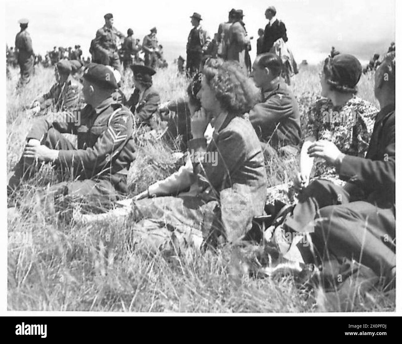 Operai di fabbrica e truppe militari assistono a una dimostrazione di paracadutismo, mettendo in evidenza l'addestramento aereo e l'impegno pubblico da parte delle forze armate. Foto Stock