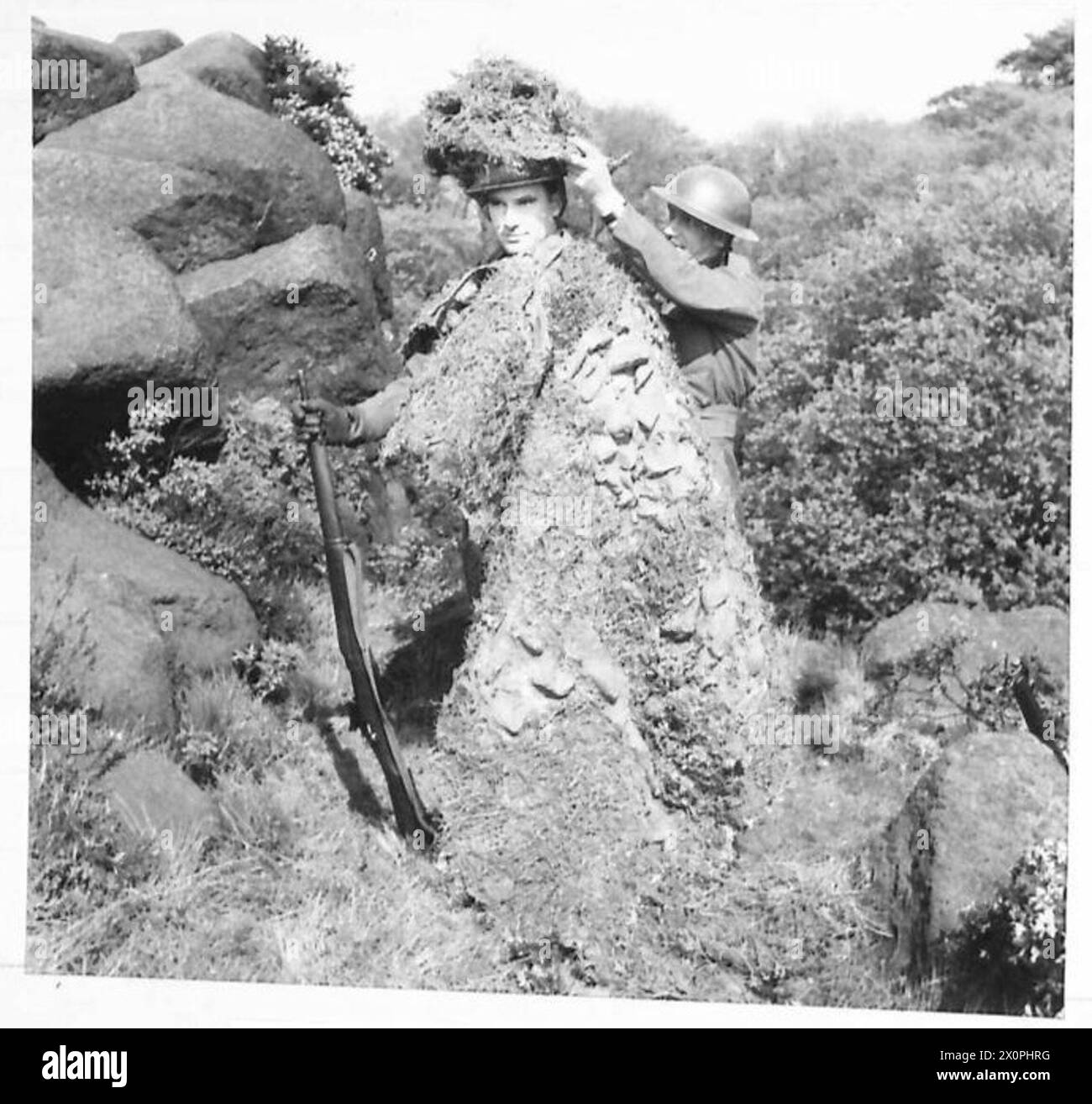 Un soldato viene aiutato a indossare un copricapo mimetico progettato per nasconderlo su uno sfondo roccioso durante gli esercizi di addestramento dei cecchini. Foto Stock