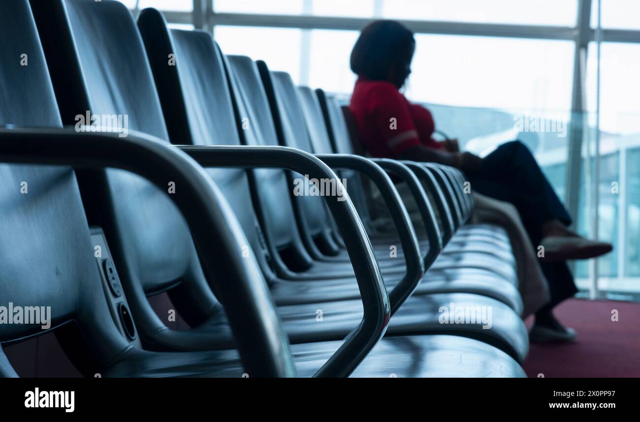 Silhouette di una donna seduta nell'area d'attesa di un terminal dell'aeroporto internazionale di Parigi. La donna osserva gli aerei in movimento attraverso la larg Foto Stock