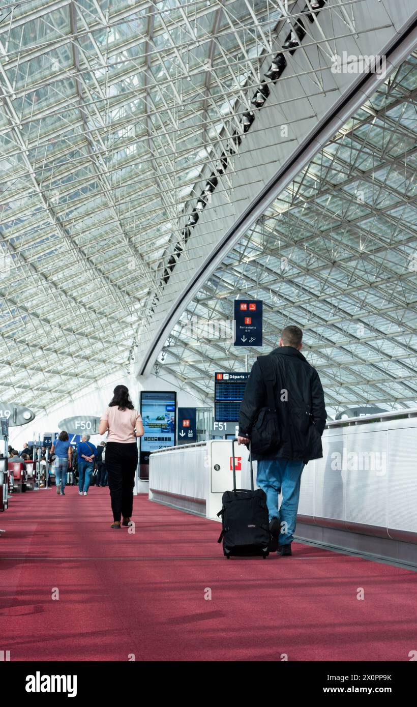 Foto retrovisiva di passeggeri con valigie all'interno di un terminal dell'aeroporto internazionale di Parigi che si avvicinano al cancello per salire a bordo dell'aereo e viaggiare. Vert Foto Stock