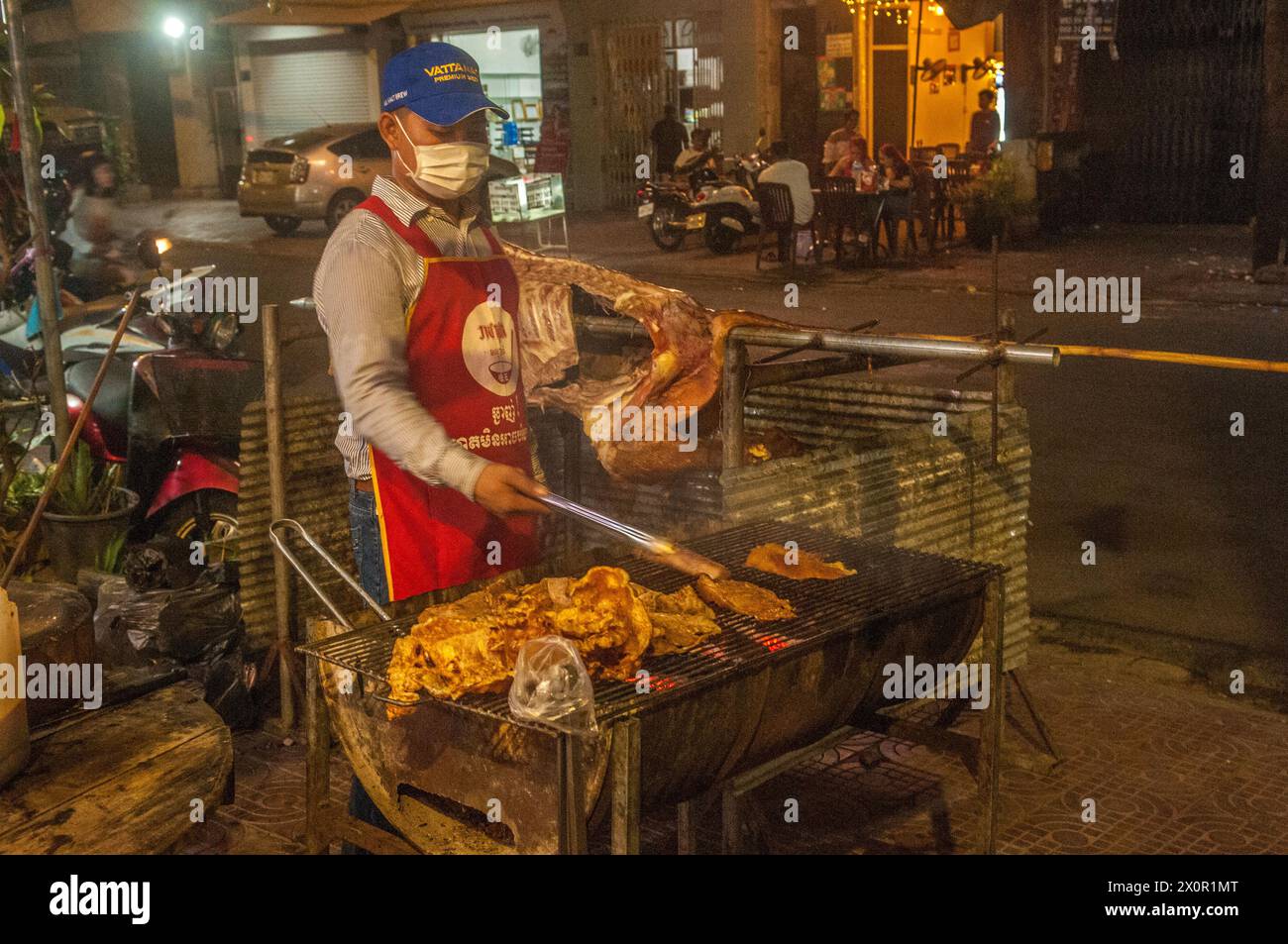 Un uomo Khmer mascherato grigia la carne in un ristorante barbecue all'aperto durante il festival cambogiano del capodanno. Phnom Penh, Cambogia. Aprile 2024. © Kraig Lieb Foto Stock