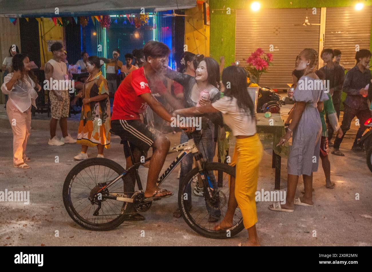 2 donne cambogiane spalmano polvere di talco / polvere bambino sul volto di un ciclista al festival cambogiano di Capodanno. Phnom Penh, Cambogia. © Kraig Lieb Foto Stock