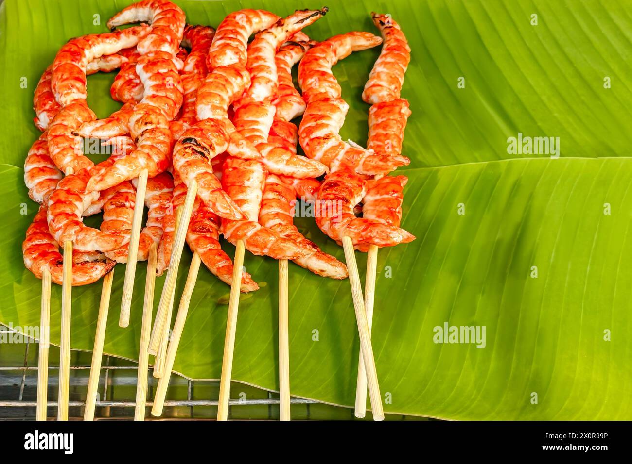 Spiedini di gamberi grigliati su verdeggianti foglie di banana con il gusto dei sapori semplici ma ricchi dello Street food. Pesce sano e appena cucinato al mercato locale exu Foto Stock