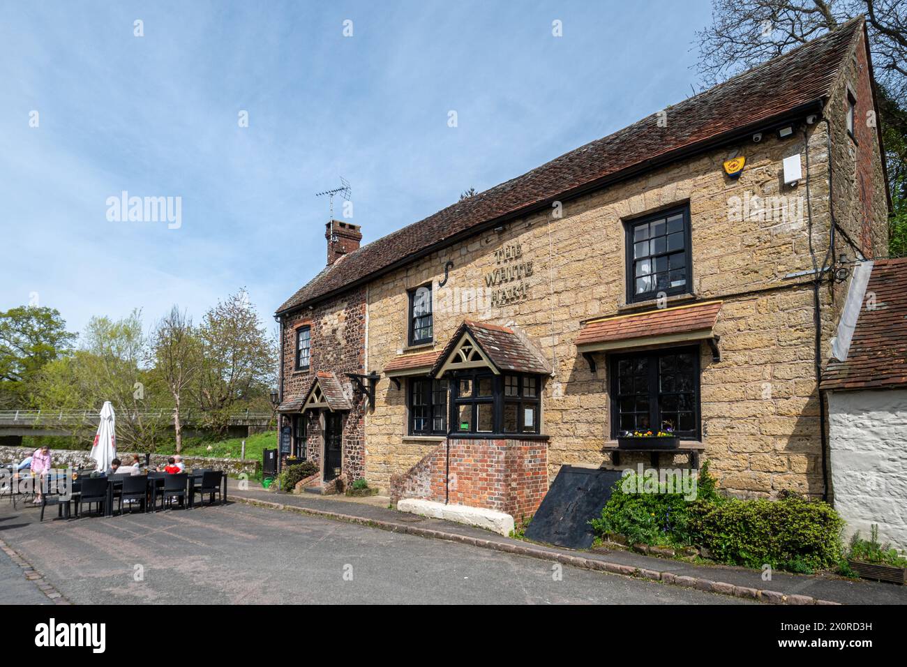 Pub White Hart con gente seduta fuori nel villaggio di Stopham, West Sussex, Inghilterra, Regno Unito Foto Stock