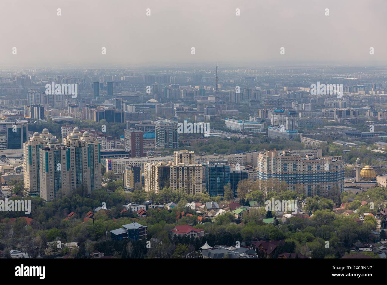 Repubblica del Kazakistan, Asia centrale. Architettura della città, spazio urbano. Vista panoramica su Almaty dal parco del monte Kok Tobe. Paesaggio urbano durante il giorno primaverile. Haze Foto Stock
