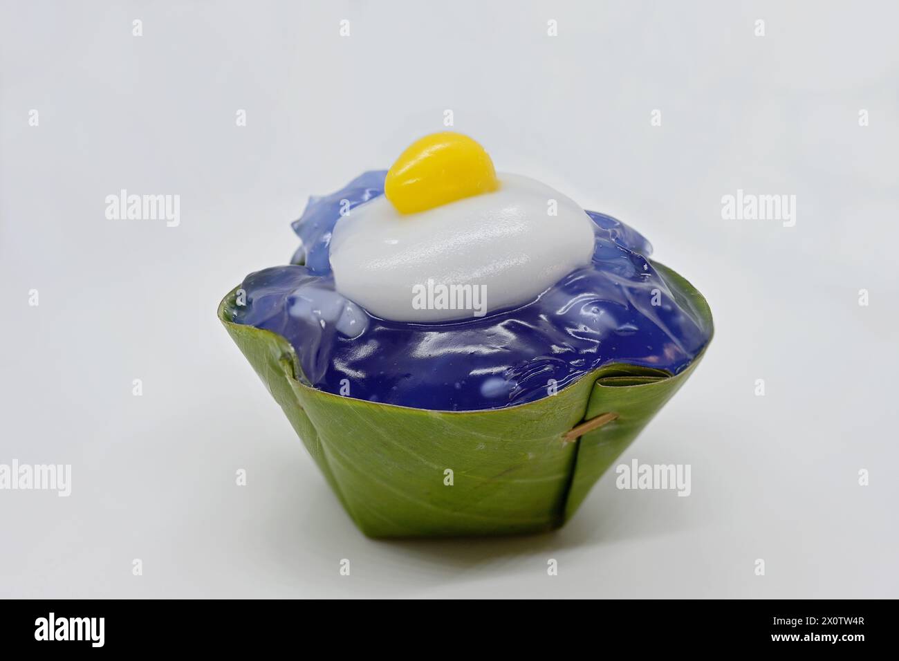 Primo piano di un dessert Khanom Tako "capovolto", con gelatina di piselli e ginkgo giallo condito con crema di cocco "Sunny-side up" in tazza di foglie di panda Foto Stock