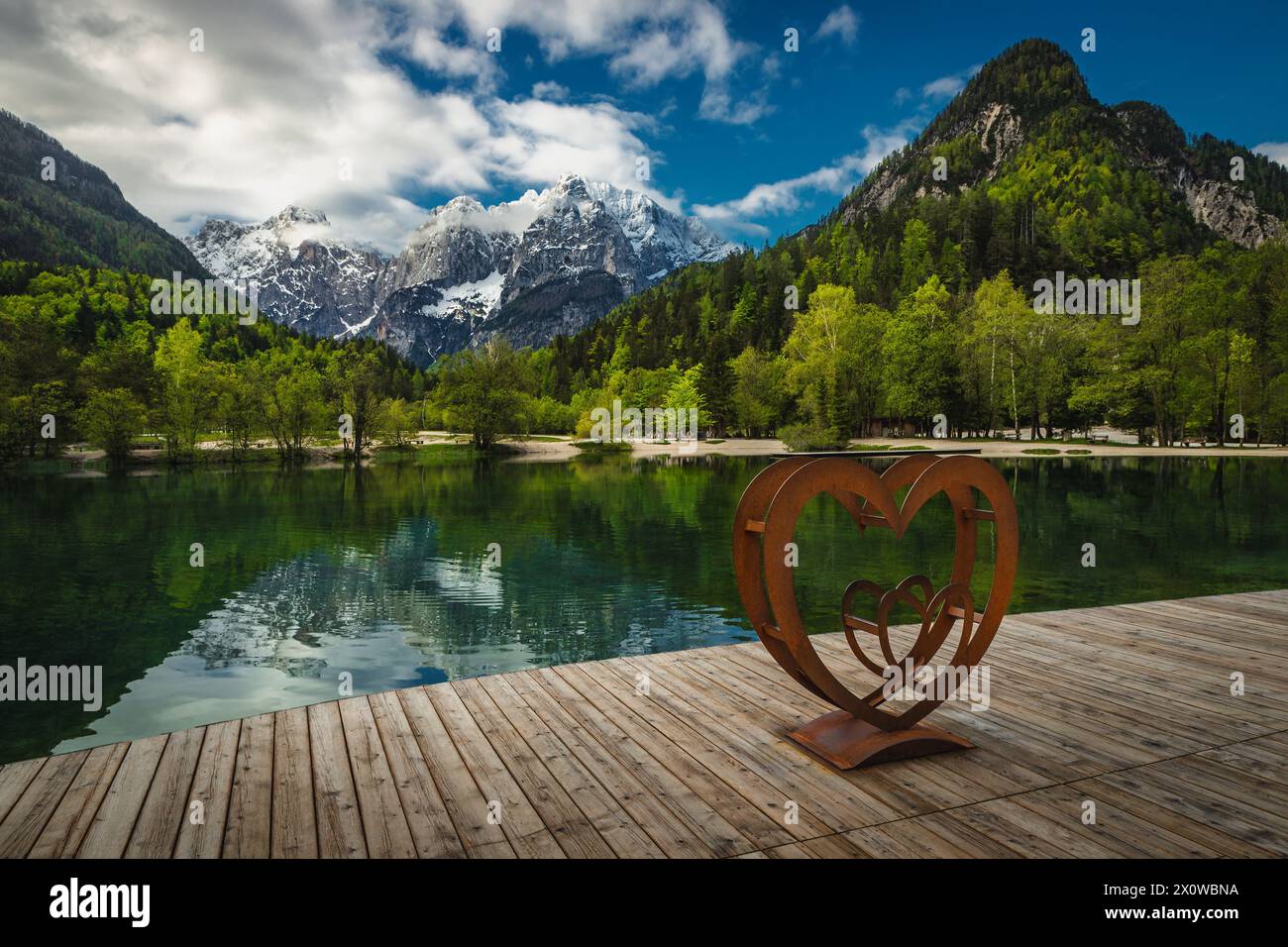 Paesaggio pittoresco con montagne innevate, foresta verde e lago pulito. Molo in legno sul lago Jasna, Kranjska Gora, Slovenia, Europa Foto Stock