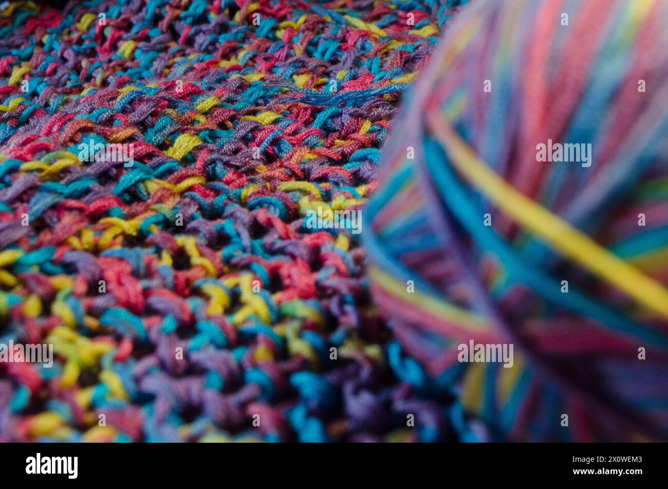 Palla di lana multicolore su una coperta all'uncinetto con profondità di campo Foto Stock