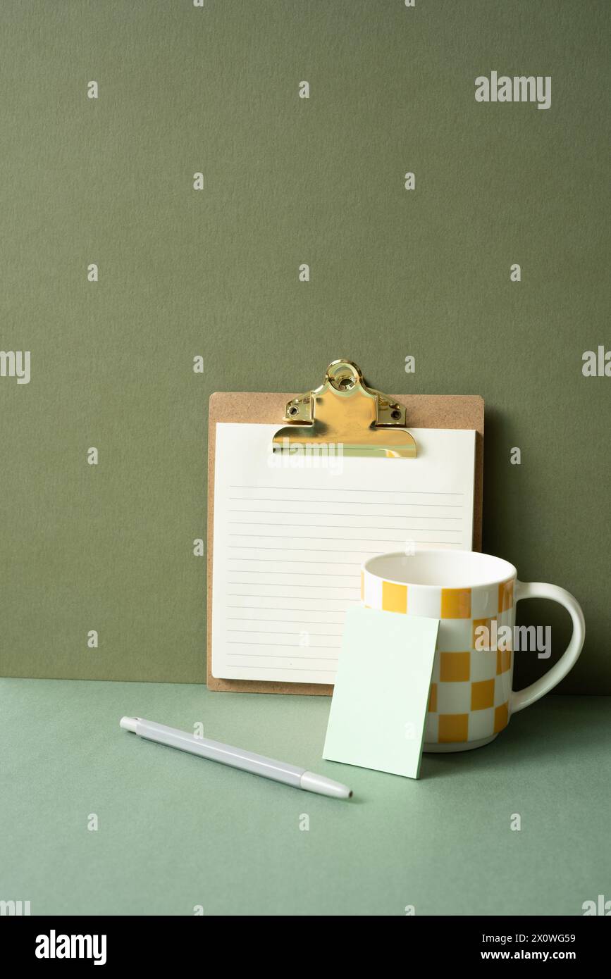 Clip legante per appunti da lavoro, penna, tazza sulla scrivania verde. sfondo parete cachi Foto Stock