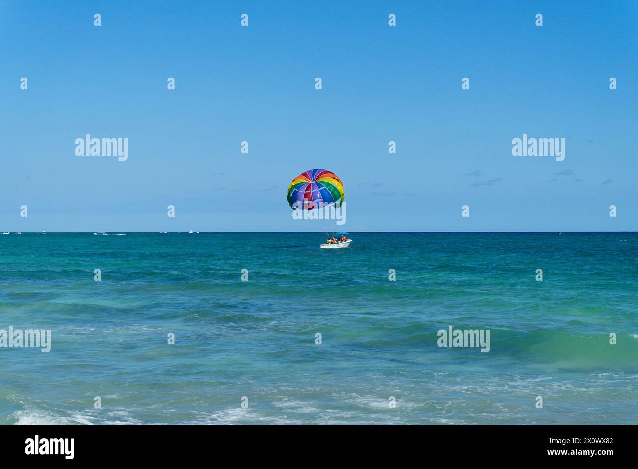 Paracadute colorato sull'oceano caraibico, legato alla barca sotto un cielo limpido. Vacanze e sport ai tropici in Messico Foto Stock