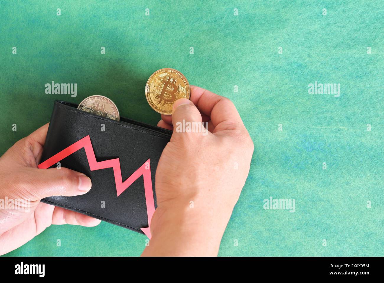 Mano umana che tiene nero un portafoglio con bitcoin e freccia rossa verso il basso e moneta all'interno. Il concetto di corsa e riduzione dei prezzi della criptovaluta. Foto Stock