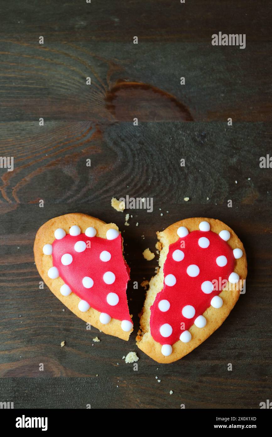 Biscotto reale a forma di glassa a forma di cuore tratteggiato rosso e bianco spezzato su sfondo nero Foto Stock