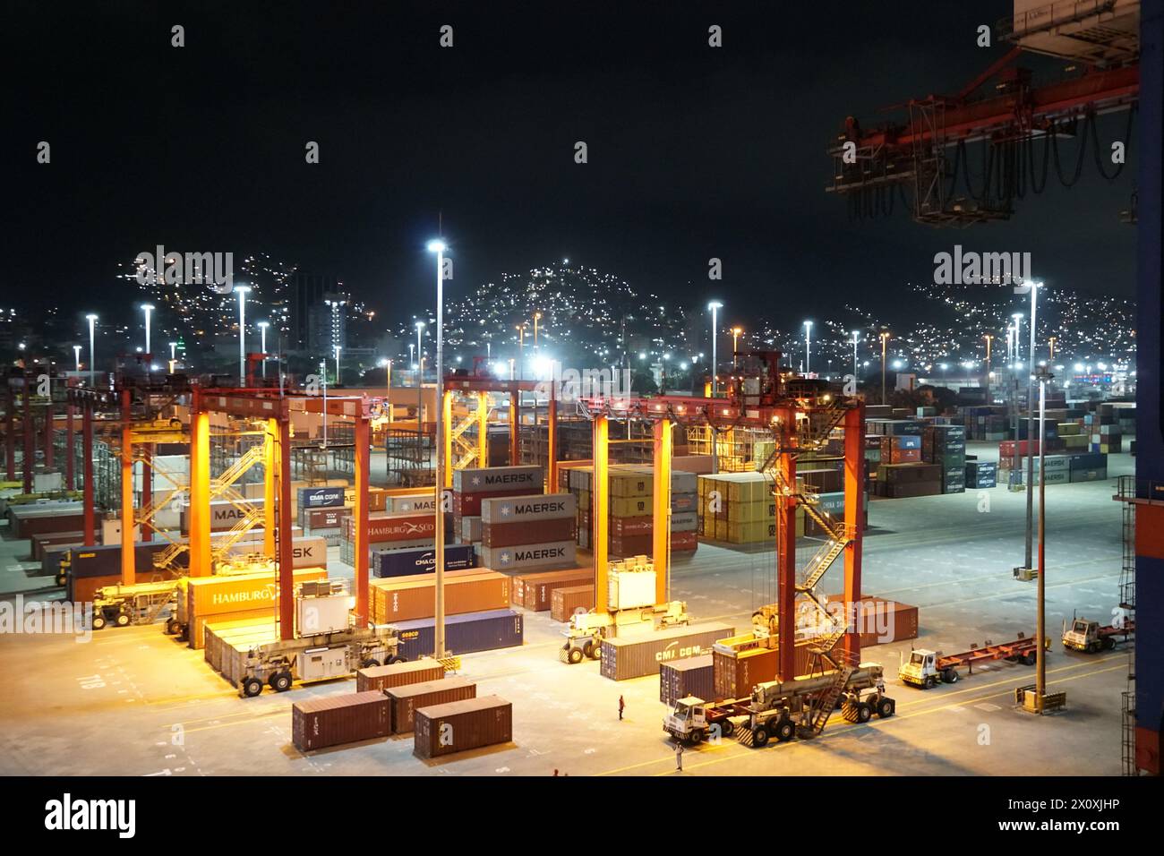 Notte nel moderno terminal container porto di la Guairá osservata dalla nave da carico ormeggiata sotto le gru a cavalletto. Foto Stock