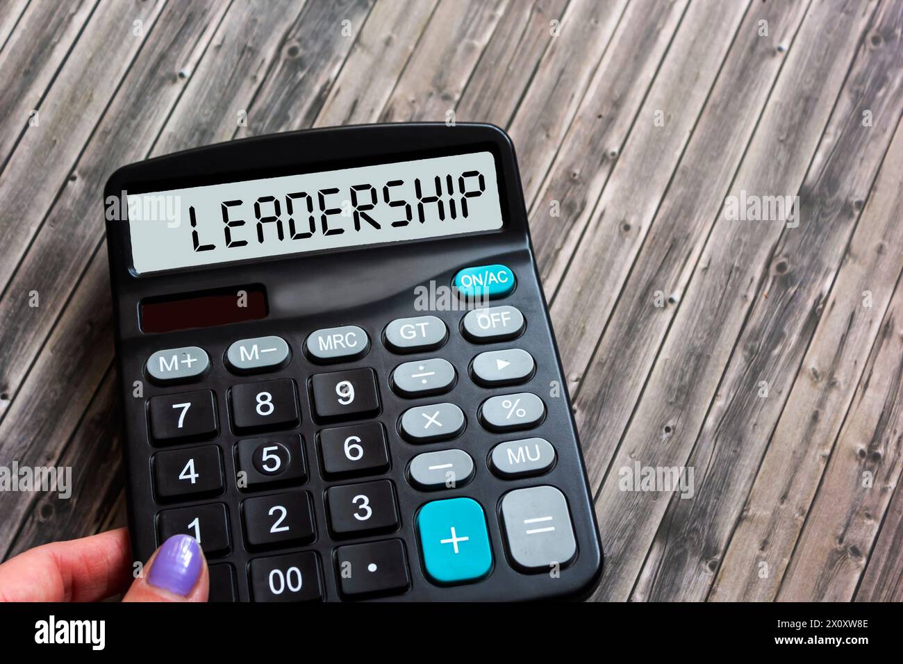 Calcolatrice nella mano di una donna che mostra la parola "leadership" su un tavolo di legno. Leadership aziendale e concetto di gestione Foto Stock