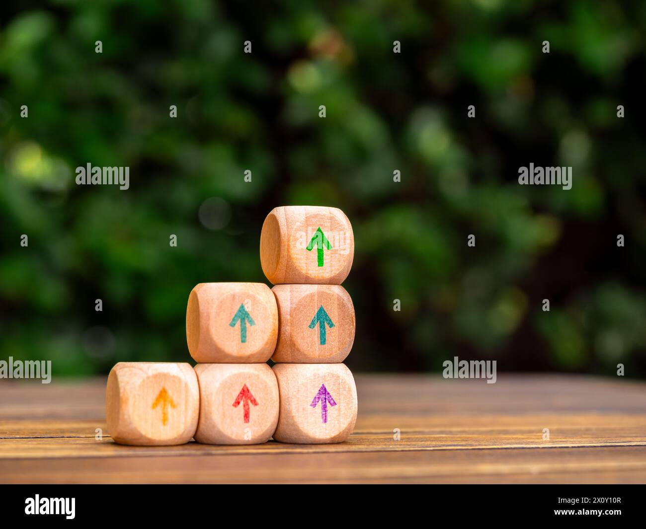 Le frecce di sollevamento multicolore su una pila di blocchi di cubo in legno, i passi del grafico a barre su sfondo verde con spazio di copia. Profitto, beneficio, reddito, ma Foto Stock
