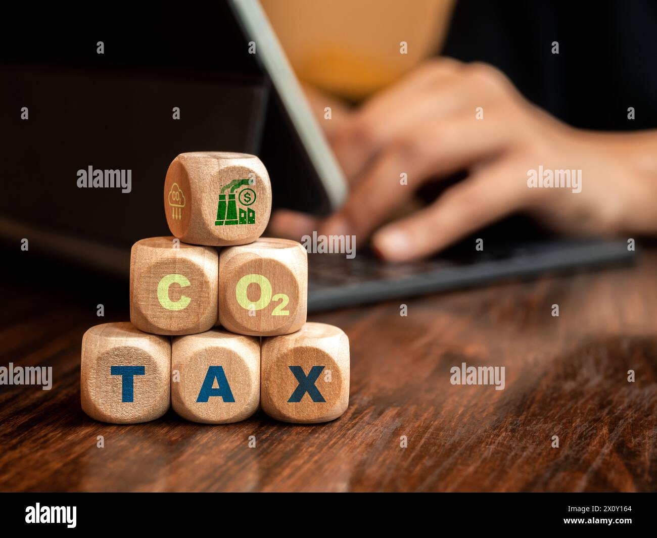 Tassa sul carbonio. Icona di una fabbrica industriale su blocchi di legno a cubo impilati con testo verde, TASSA CO2 sulla scrivania con uomo d'affari con notebook. Ambientale, sociale Foto Stock