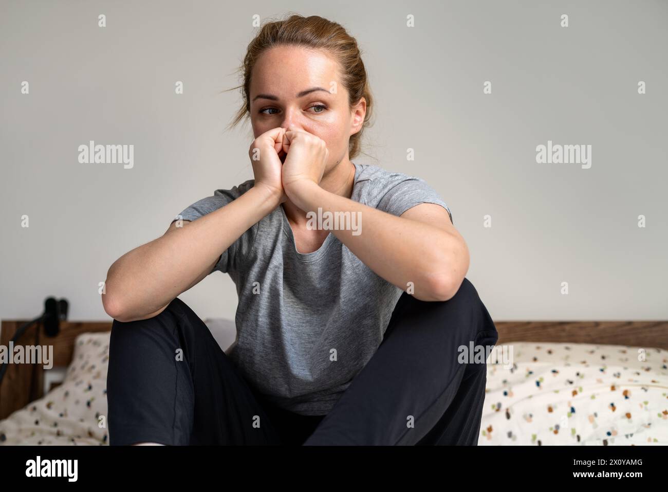 Donna adulta depressa e degradata a casa. Una donna infelice si siede sul letto a casa. Foto Stock