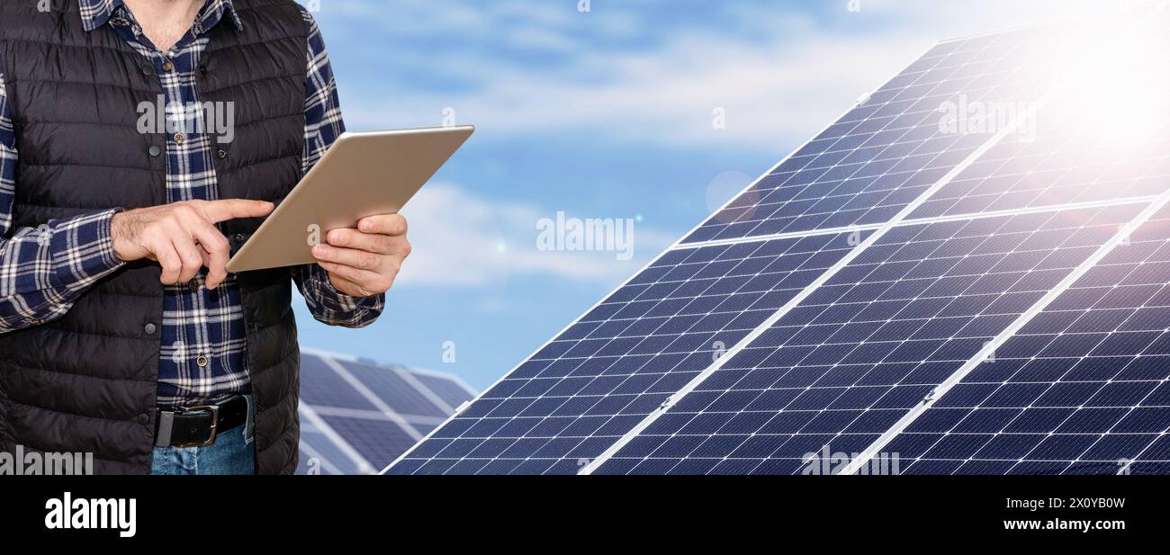 Operaio di impianti a energia solare che utilizza un tablet digitale sullo sfondo di pannelli solari industriali. Foto Stock
