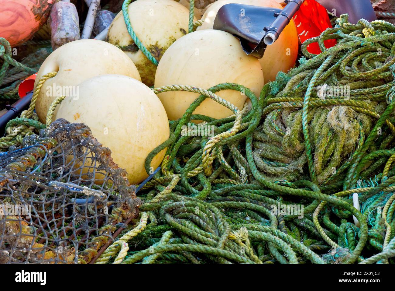 Primo piano di un mucchio di attrezzi da pesca costiera ammassati sulla banchina del porto di Arbroath, canne, vasi di granchio o aragosta, corde, galleggianti e bandiere segnaletiche. Foto Stock