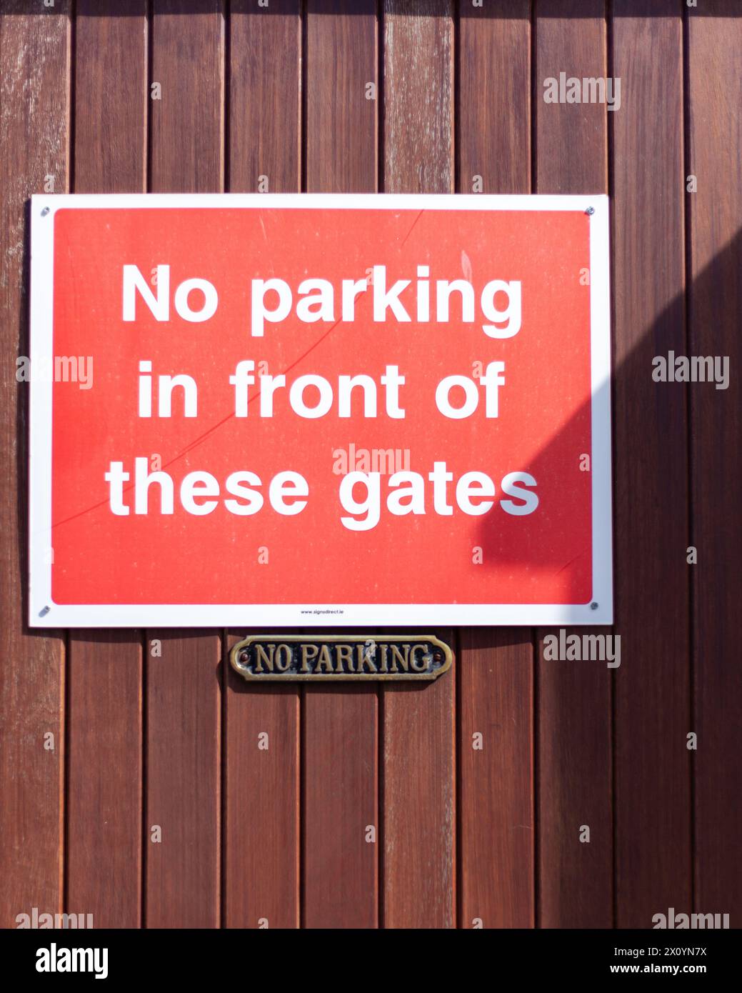 Due segnali di divieto di parcheggio su un cancello di legno in una giornata di sole. C'è un'ombra di un tetto sul cartello Foto Stock
