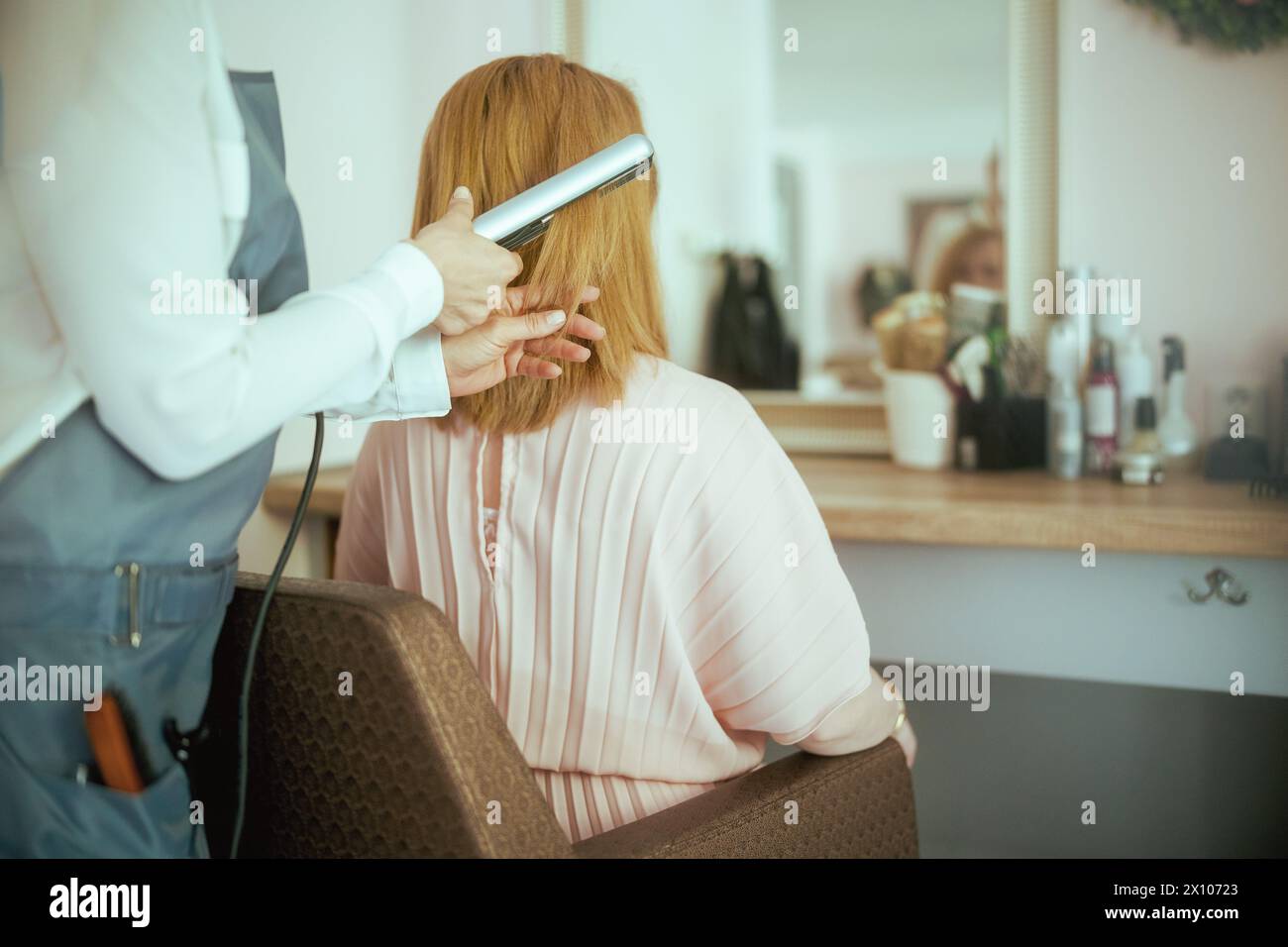 Vista da dietro parrucchiere donna in un moderno salone di bellezza con piastra per capelli e cliente. Foto Stock