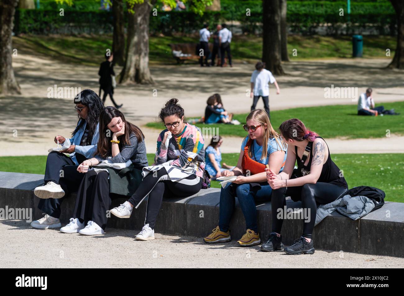 Etterbeek, Bruxelles, Belgio - 13 aprile 2024 - persone sedute alla fontana del parco del Cinquantenario al sole Foto Stock