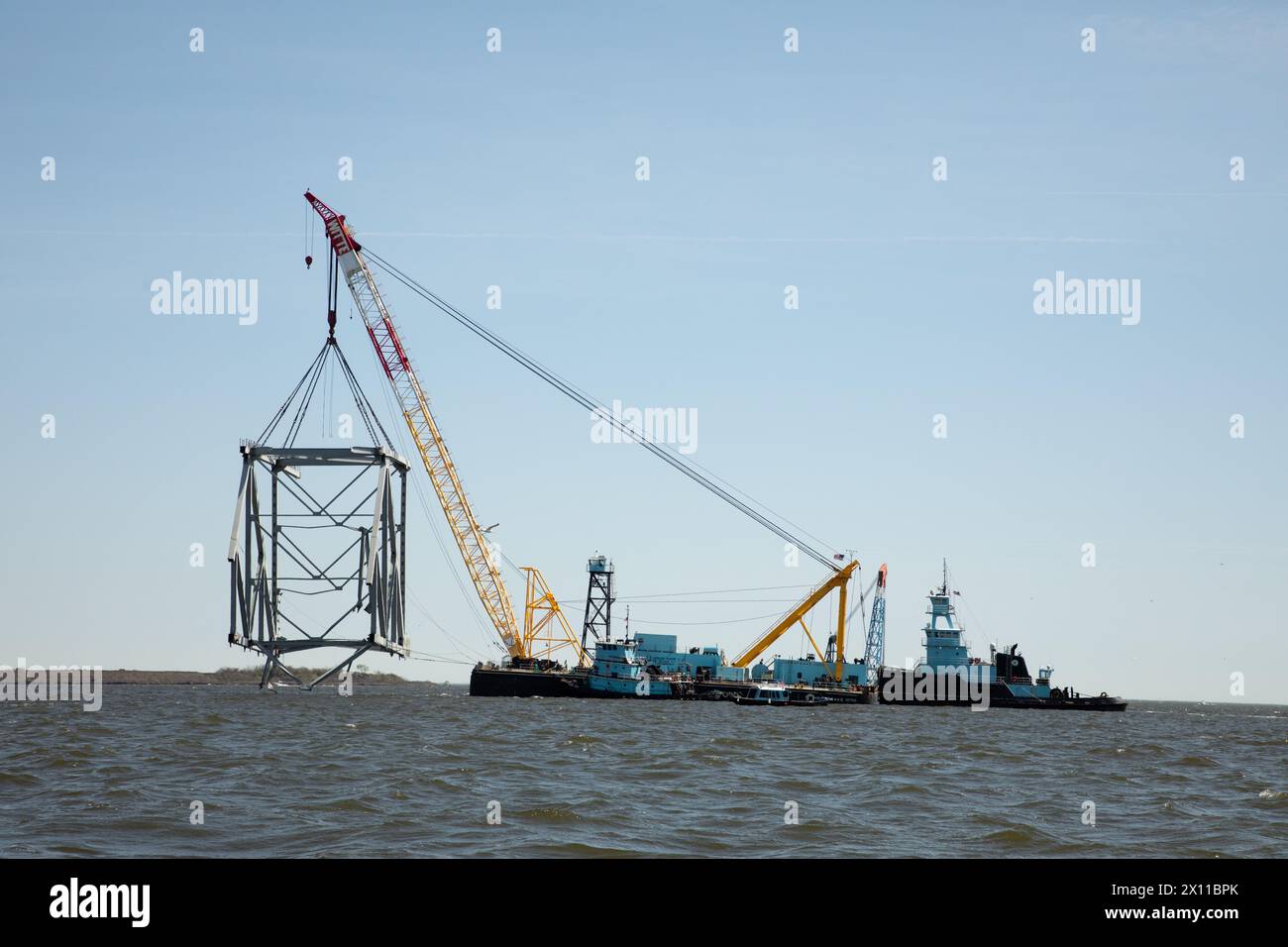 Key Bridge Response 2024 i salvatori dello Unified Command utilizzano la chiatta della gru Chesapeake 1000, per spostare un grande pezzo di acciaio di supporto dal crollato Francis Scott Key Bridge, 14 aprile 2024, a Baltimora, Maryland. La Chesapeake 1000 è la più grande gru galleggiante sulla costa orientale, e la rimozione di questi grandi pezzi aiuterà ad aprire un canale ad accesso limitato che consente il traffico di navi a senso unico verso il porto di Baltimora. La rimozione di detriti e rottami è in corso a sostegno di una priorità assoluta per aprire in modo sicuro ed efficiente il canale di Fort McHenry. Foto Stock