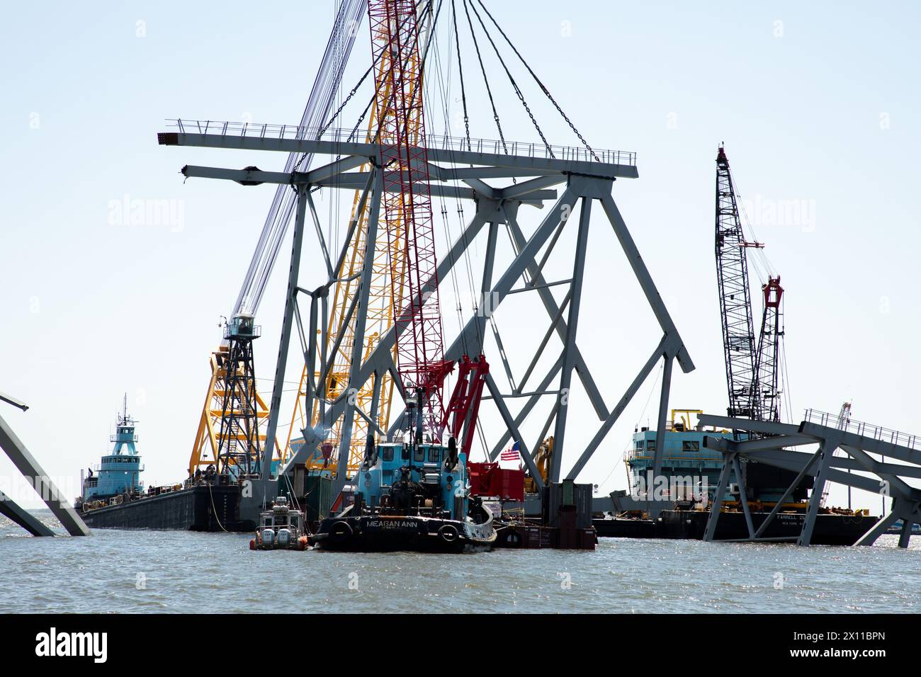 Key Bridge Response 2024 i salvatori dello Unified Command utilizzano la chiatta della gru Chesapeake 1000, per spostare un grande pezzo di acciaio di supporto dal crollato Francis Scott Key Bridge, 14 aprile 2024, a Baltimora, Maryland. La Chesapeake 1000 è la più grande gru galleggiante sulla costa orientale, e la rimozione di questi grandi pezzi aiuterà ad aprire un canale ad accesso limitato che consente il traffico di navi a senso unico verso il porto di Baltimora. La rimozione di detriti e rottami è in corso a sostegno di una priorità assoluta per aprire in modo sicuro ed efficiente il canale di Fort McHenry. Foto Stock
