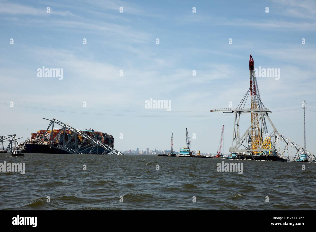 Key Bridge Response 2024 i salvatori dello Unified Command utilizzano la chiatta della gru Chesapeake 1000, per spostare un grande pezzo di acciaio di supporto dal crollato Francis Scott Key Bridge, 14 aprile 2024, a Baltimora, Maryland. La Chesapeake 1000 è la più grande gru galleggiante sulla costa orientale, e la rimozione di questi grandi pezzi aiuterà ad aprire un canale ad accesso limitato che consente il traffico di navi a senso unico verso il porto di Baltimora. La rimozione di detriti e rottami è in corso a sostegno di una priorità assoluta per aprire in modo sicuro ed efficiente il canale di Fort McHenry. Foto Stock