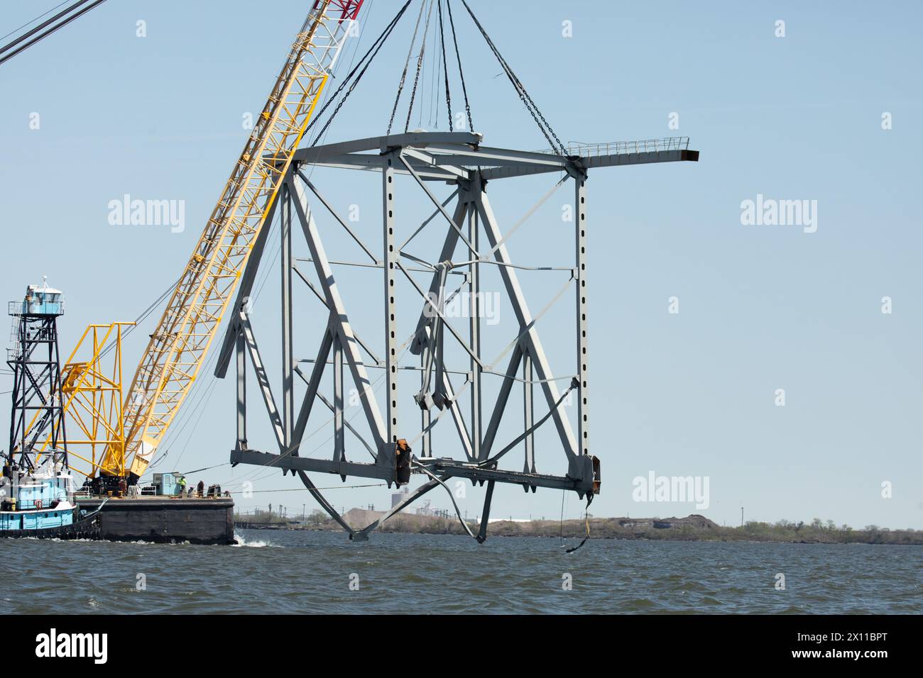 Key Bridge Response 2024 i salvatori dello Unified Command utilizzano la chiatta della gru Chesapeake 1000, per spostare un grande pezzo di acciaio di supporto dal crollato Francis Scott Key Bridge, 14 aprile 2024, a Baltimora, Maryland. La Chesapeake 1000 è la più grande gru galleggiante sulla costa orientale, e la rimozione di questi grandi pezzi aiuterà ad aprire un canale ad accesso limitato che consente il traffico di navi a senso unico verso il porto di Baltimora. La rimozione di detriti e rottami è in corso a sostegno di una priorità assoluta per aprire in modo sicuro ed efficiente il canale di Fort McHenry. Foto Stock