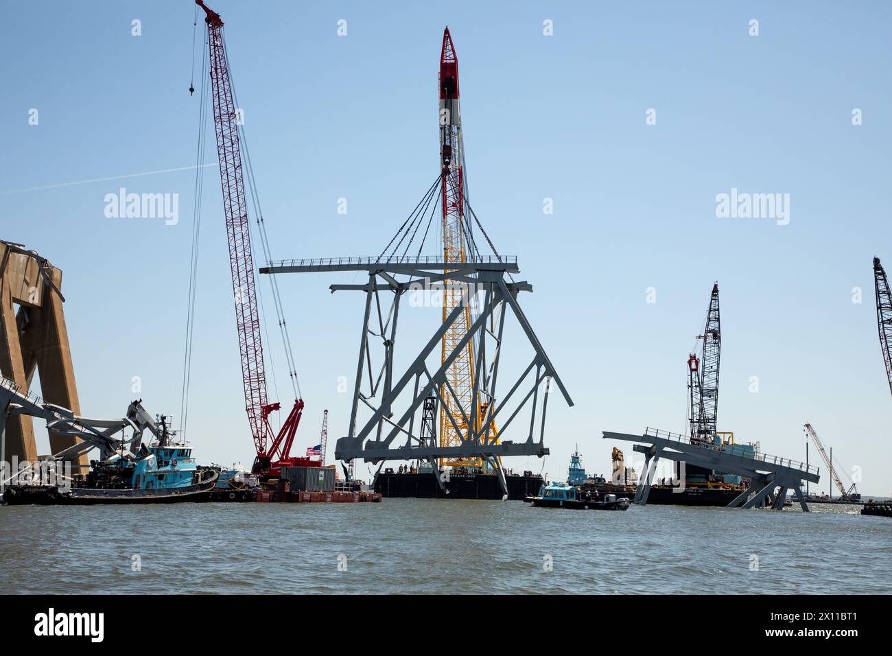 Key Bridge Response 2024 i salvatori dello Unified Command utilizzano la chiatta della gru Chesapeake 1000, per spostare un grande pezzo di acciaio di supporto dal crollato Francis Scott Key Bridge, 14 aprile 2024, a Baltimora, Maryland. La Chesapeake 1000 è la più grande gru galleggiante sulla costa orientale, e la rimozione di questi grandi pezzi aiuterà ad aprire un canale ad accesso limitato che consente il traffico di navi a senso unico verso il porto di Baltimora. La rimozione di detriti e rottami è in corso a sostegno di una priorità assoluta per aprire in modo sicuro ed efficiente il canale di Fort McHenry. Foto Stock