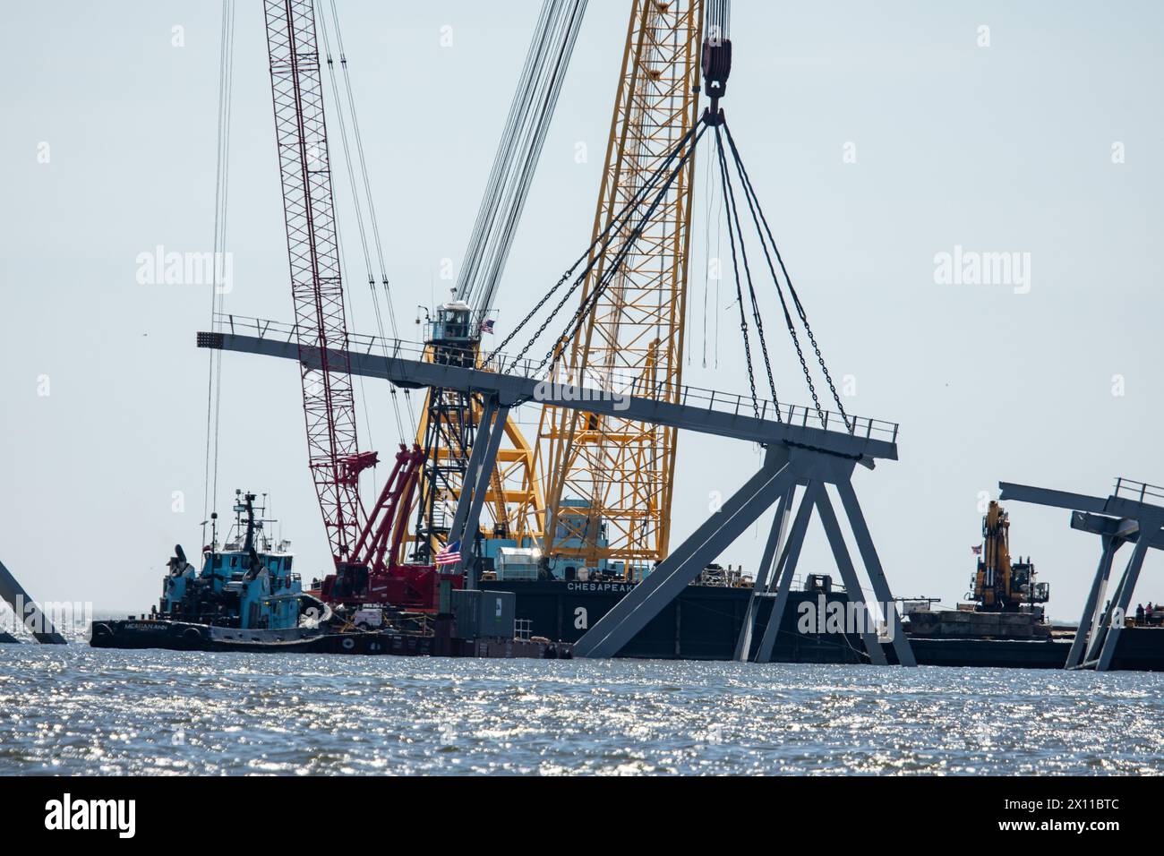 Key Bridge Response 2024 i salvatori dello Unified Command utilizzano la chiatta della gru Chesapeake 1000, per spostare un grande pezzo di acciaio di supporto dal crollato Francis Scott Key Bridge, 14 aprile 2024, a Baltimora, Maryland. La Chesapeake 1000 è la più grande gru galleggiante sulla costa orientale, e la rimozione di questi grandi pezzi aiuterà ad aprire un canale ad accesso limitato che consente il traffico di navi a senso unico verso il porto di Baltimora. La rimozione di detriti e rottami è in corso a sostegno di una priorità assoluta per aprire in modo sicuro ed efficiente il canale di Fort McHenry. Foto Stock