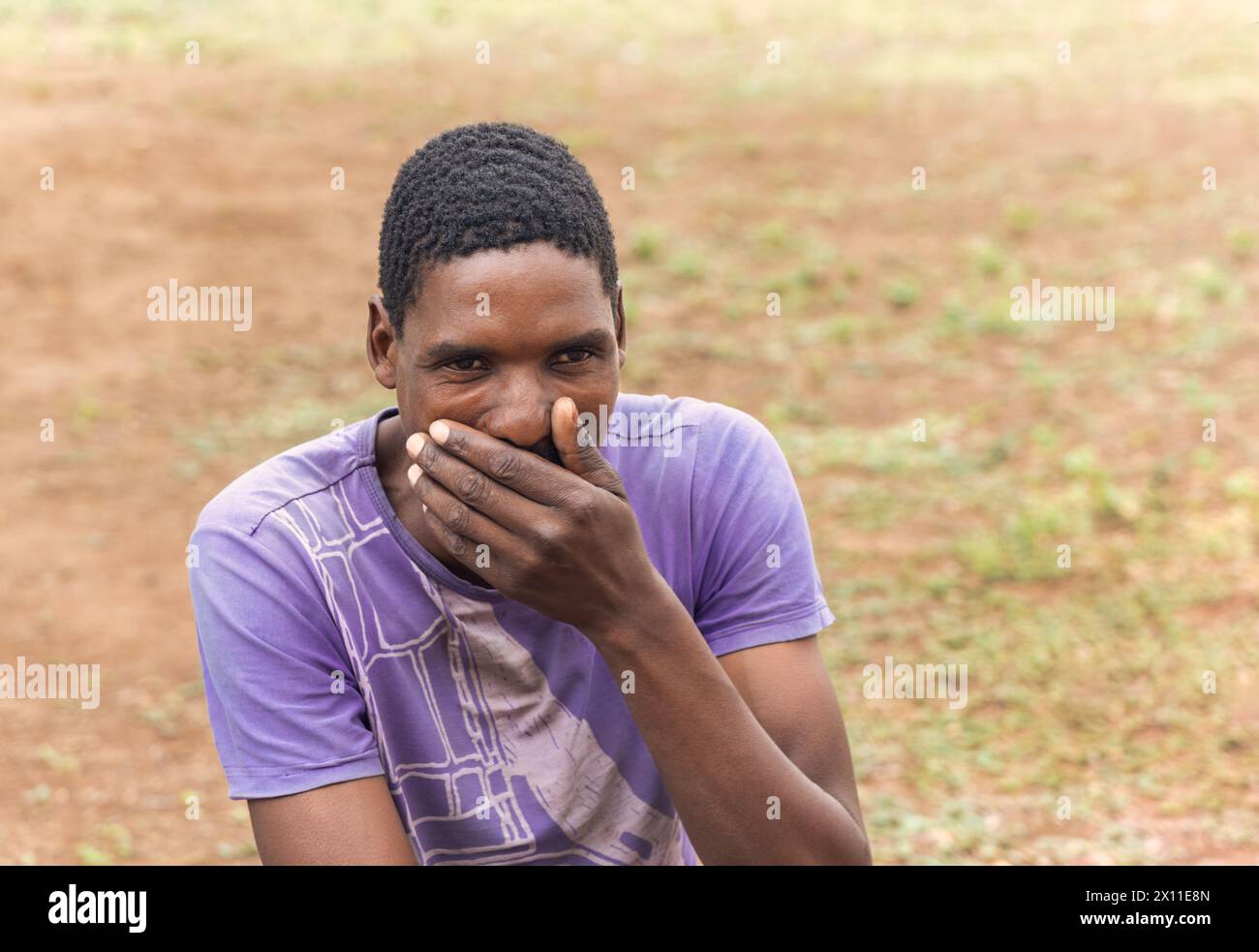 ritratto di un uomo africano che tiene la mano sulla bocca, reazione sorpresa, nel cortile del villaggio Foto Stock