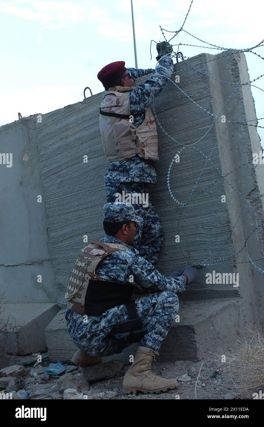 Due poliziotti nazionali iracheni con il 1st Battalion, la 2nd Brigade, la 6th Iraqi National Police piazzano filo a concertina vicino ad un ponte a Kahdra CA. 2004 Foto Stock