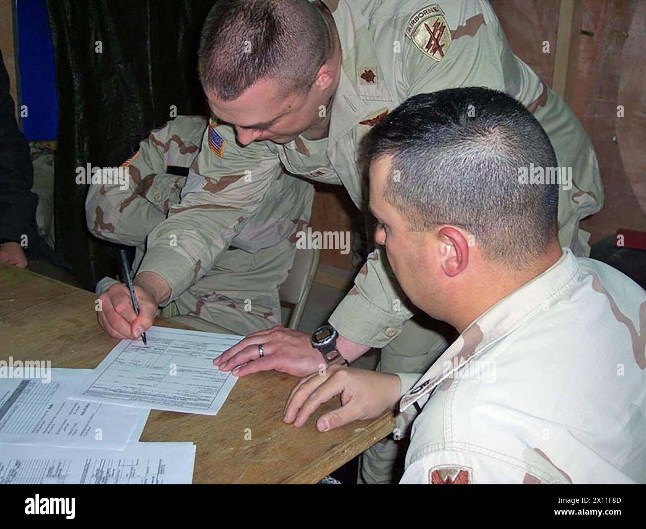 Un ufficiale pagatore con il 1088esimo Ing. BN. Del 256th Brigade Combat Team che osserva il maggiore David Langfellow, comandante di Un Co. 407th Civil Affairs BN., mentre firma alcuni documenti per pagare un appaltatore locale per il suo lavoro su un progetto di gasdotto. Il progetto faceva parte della missione di portare una migliore qualità della vita alla popolazione della zona di Mahmudiyah Iraq CA. 1° febbraio 2004 Foto Stock