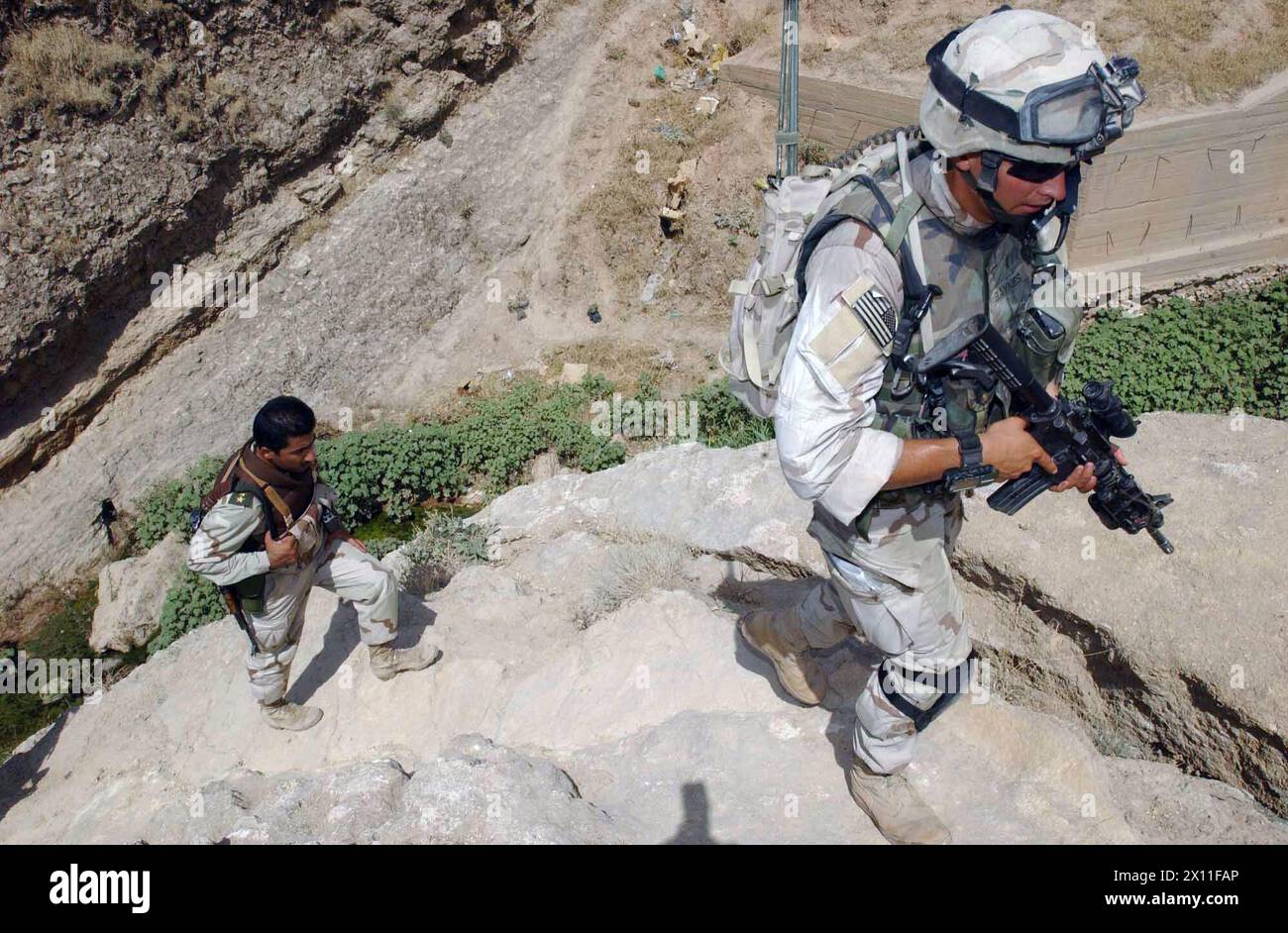 Il tenente William Baynes e un ufficiale della Guardia Nazionale irachena salgono su una collina a Tall Afar, Iraq, dopo aver cercato un fosso fognario per le miniere e gli ordigni inesplosi. Durante un'operazione di prima mattina il 1 agosto 2004, tre battaglioni della 3rd Brigade, 2nd Infantry Division (Stryker Brigade Combat Team) e tre battaglioni della Guardia Nazionale irachena hanno condotto cordone e perquisizioni congiunte attraverso la città occidentale della provincia di Ninevah nel tentativo di sequestrare armi e trattenere i terroristi in cerca di rifugio in città. Foto Stock