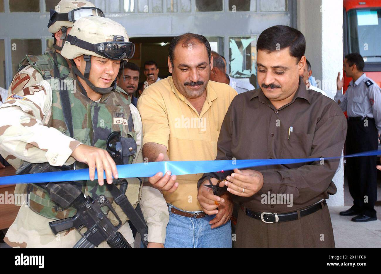 Il capitano Marc Chung (a sinistra) 425th Civil Affairs Battalion, l'appaltatore iracheno responsabile delle riparazioni di restauro (centro) e il colonnello Waleed si preparano a tagliare un nastro per commemorare il rinnovamento della stazione dei vigili del fuoco di Amariya CA. 8 maggio 2004 Foto Stock