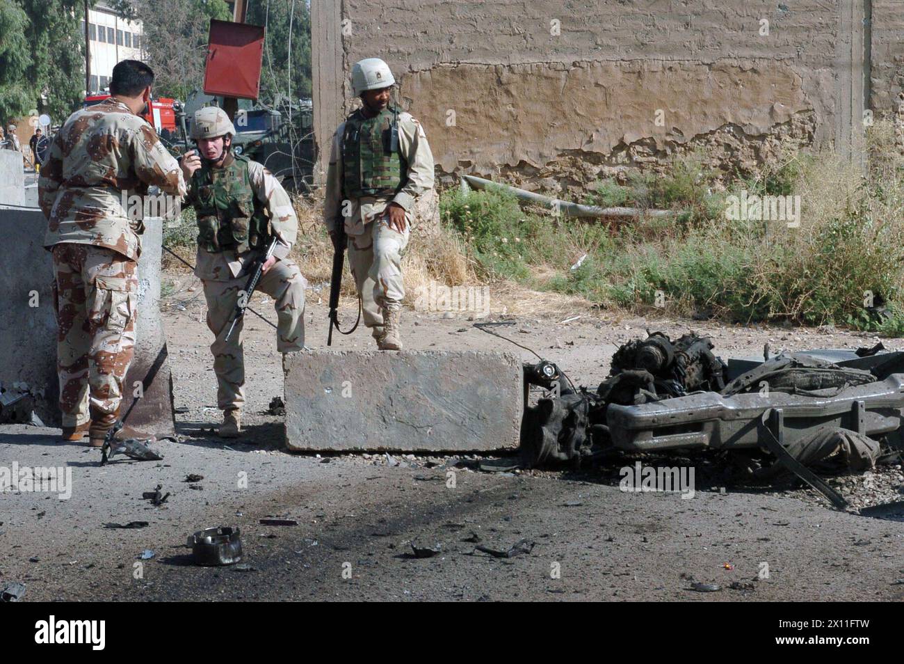 Le forze multinazionali lavorano con la Guardia Nazionale irachena per proteggere il sito di un ordigno esplosivo improvvisato trasportato da veicoli il 26 luglio 2004. Quattro iracheni sono stati uccisi, tra cui una donna e un bambino, un dipendente dei servizi di protezione delle strutture e l'attentatore suicida. Il veicolo è esploso a 50 metri dal cancello principale dell'aeroporto di Mosul, una base delle forze multinazionali a Mosul, Iraq. Era caricato con razzi da 122 mm e un mortaio da 60 mm che non detonò nell'esplosione. La scena fu messa in sicurezza e furono inviate squadre di ordigni esplosivi per smaltire le munizioni. Foto Stock
