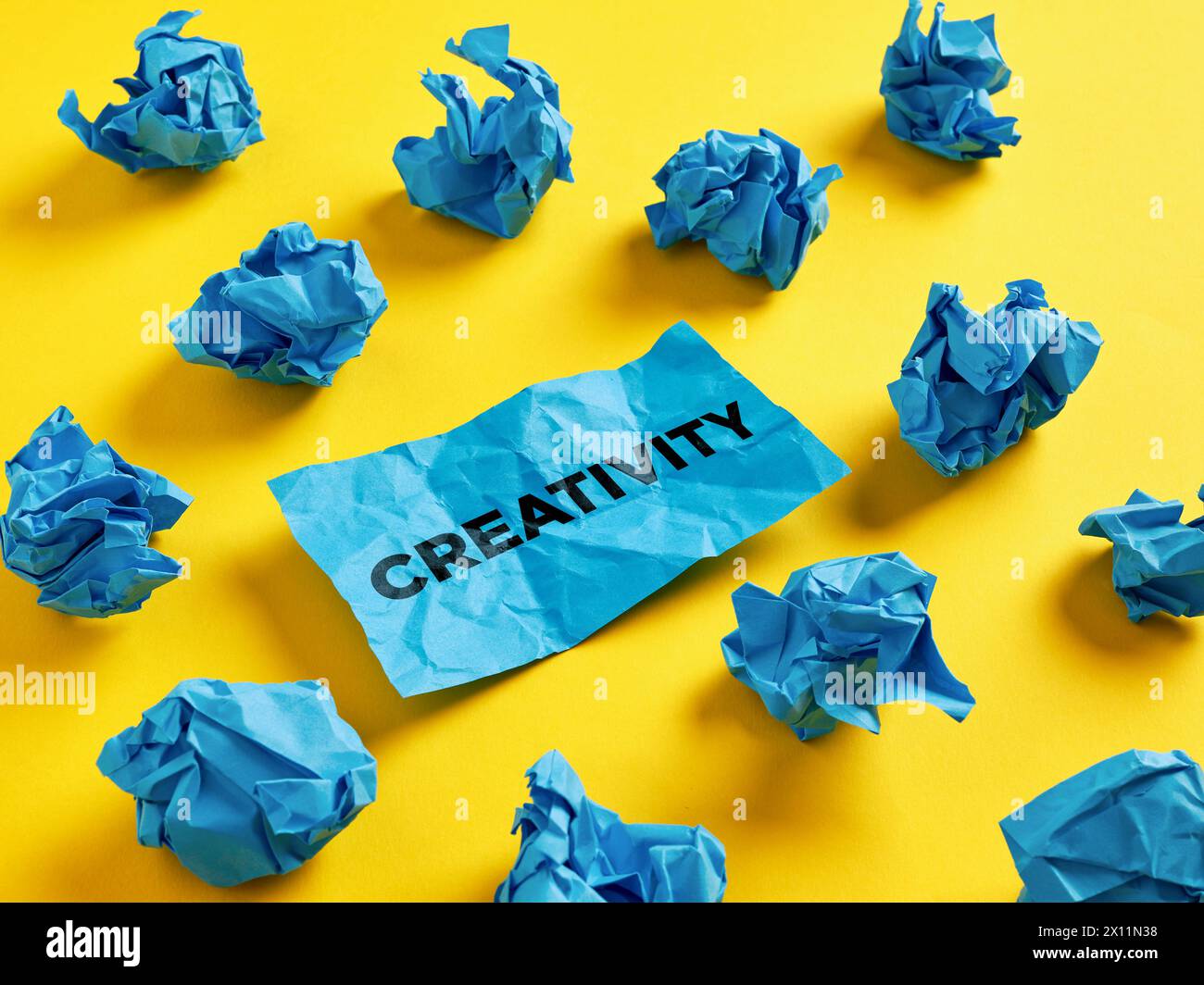 Brainstorming per trovare un'idea creativa, una soluzione o una creatività. La parola creatività su un pezzo di carta tra le palline di carta blu. Foto Stock