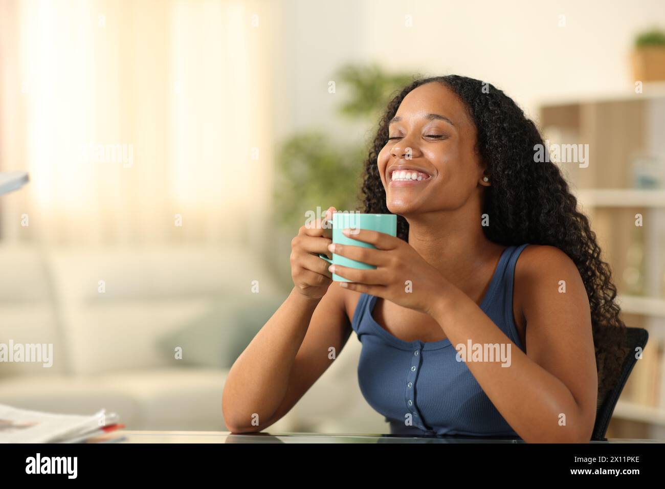 Donna nera felice che si gode il caffè profumato e sorride seduta a casa Foto Stock