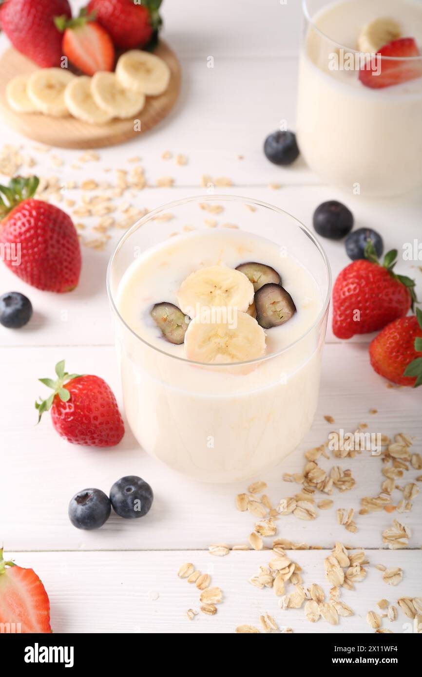 Pausa salutare. Composizione con gustoso yogurt, banana e frutti di bosco in bicchieri su tavolo di legno bianco Foto Stock