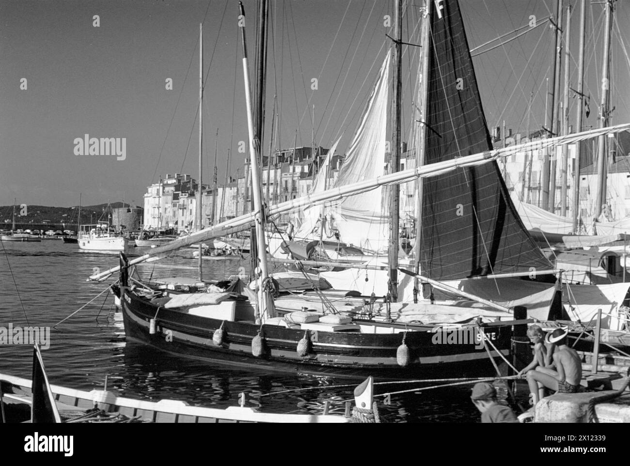 Due ragazzi che praticano la pesca e gli storici yacht in legno nel vecchio porto Saint Tropez o St Tropez Var Côte d'Azur o Costa Azzurra Francia. Immagine vintage o storica c1960 Foto Stock