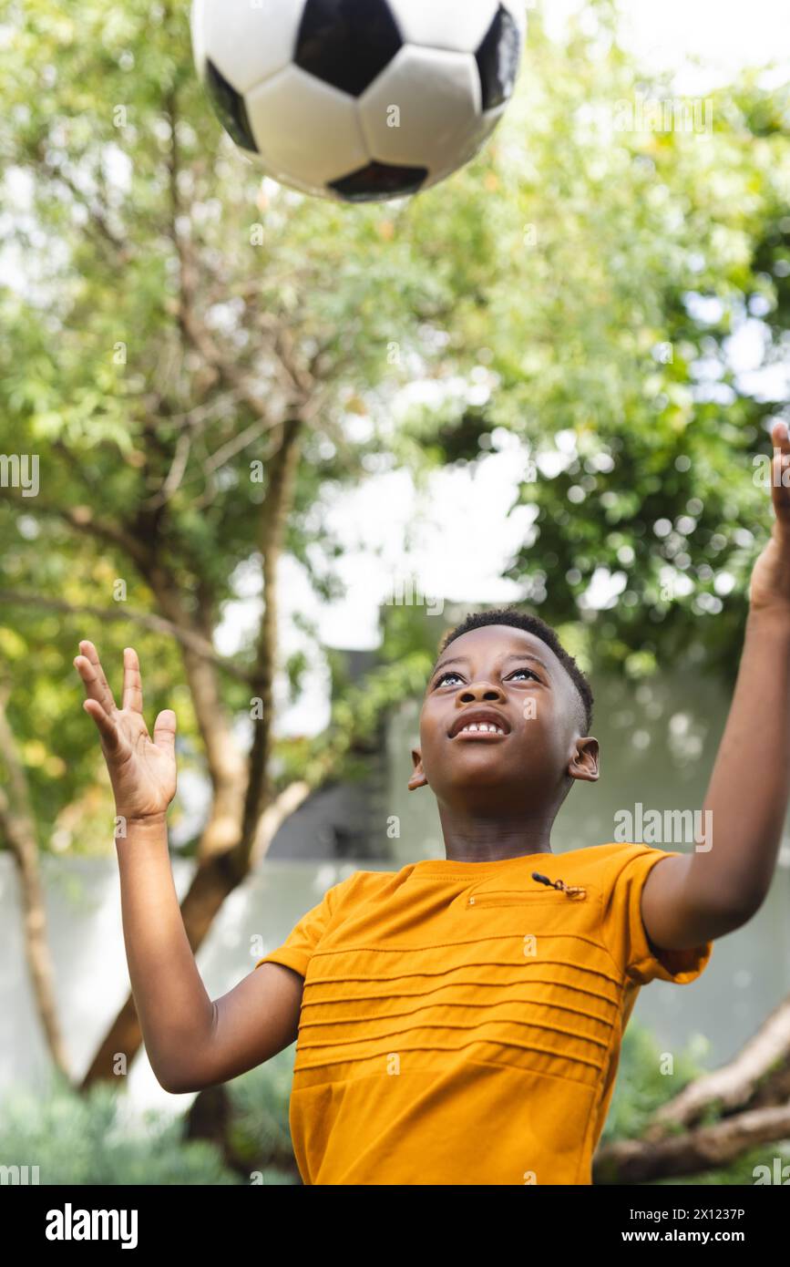 Ragazzo afroamericano che gioca con la palla da calcio, alberi verdi sullo sfondo Foto Stock