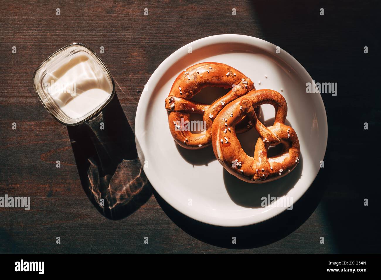 Un bicchiere di yogurt e due pretzel su un piatto sul tavolo la mattina, attenzione selettiva Foto Stock