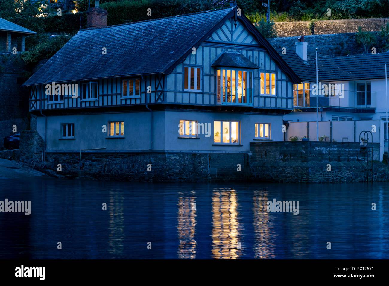 Luce serale a Warfleet Creek. Luci della casa e riflessioni acquatiche da un cottage Riverside, Dartmouth Foto Stock