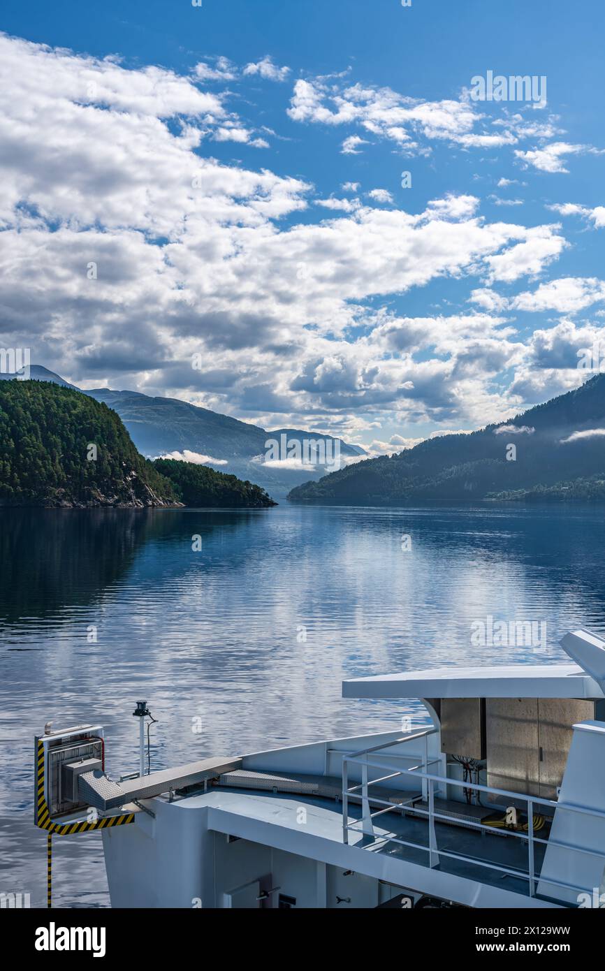 Un traghetto naviga attraverso le calme acque del fiordo, con montagne e nuvole bianche in una giornata estiva di sole a Stangvikfjord in Norvegia Foto Stock