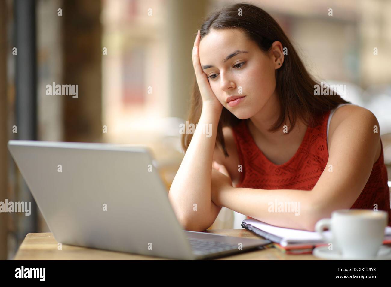 Studente apatico che guarda contenuti online su un computer portatile nella terrazza di un bar Foto Stock