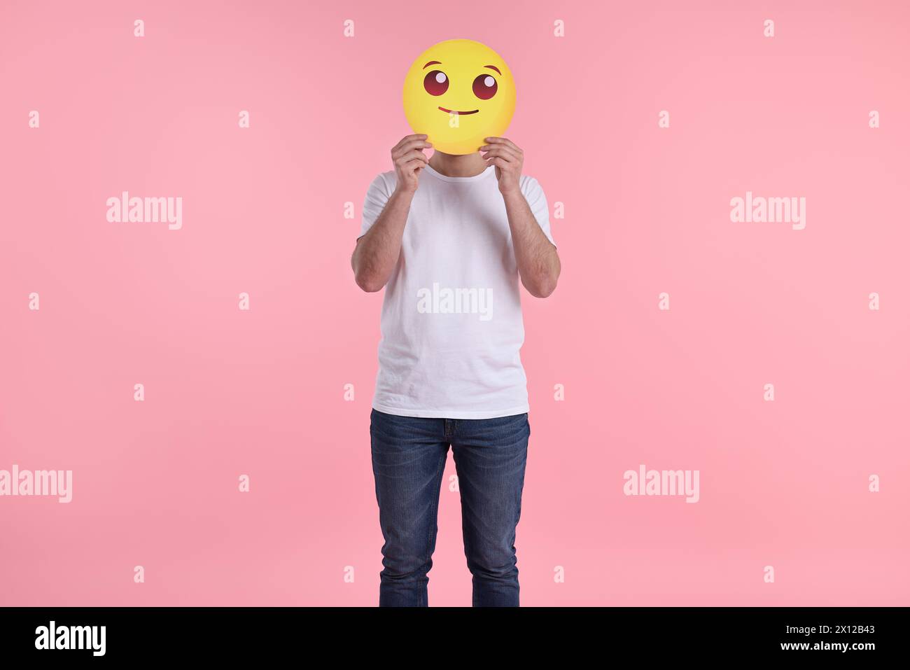 Uomo che copre il viso con emoticon sorridente su sfondo rosa Foto Stock