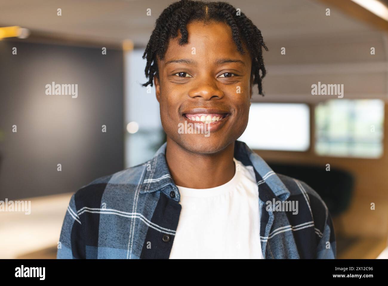 Uomo afroamericano in piedi, con una camicia a quadri, sorridendo davanti alla macchina fotografica in un moderno ufficio aziendale Foto Stock