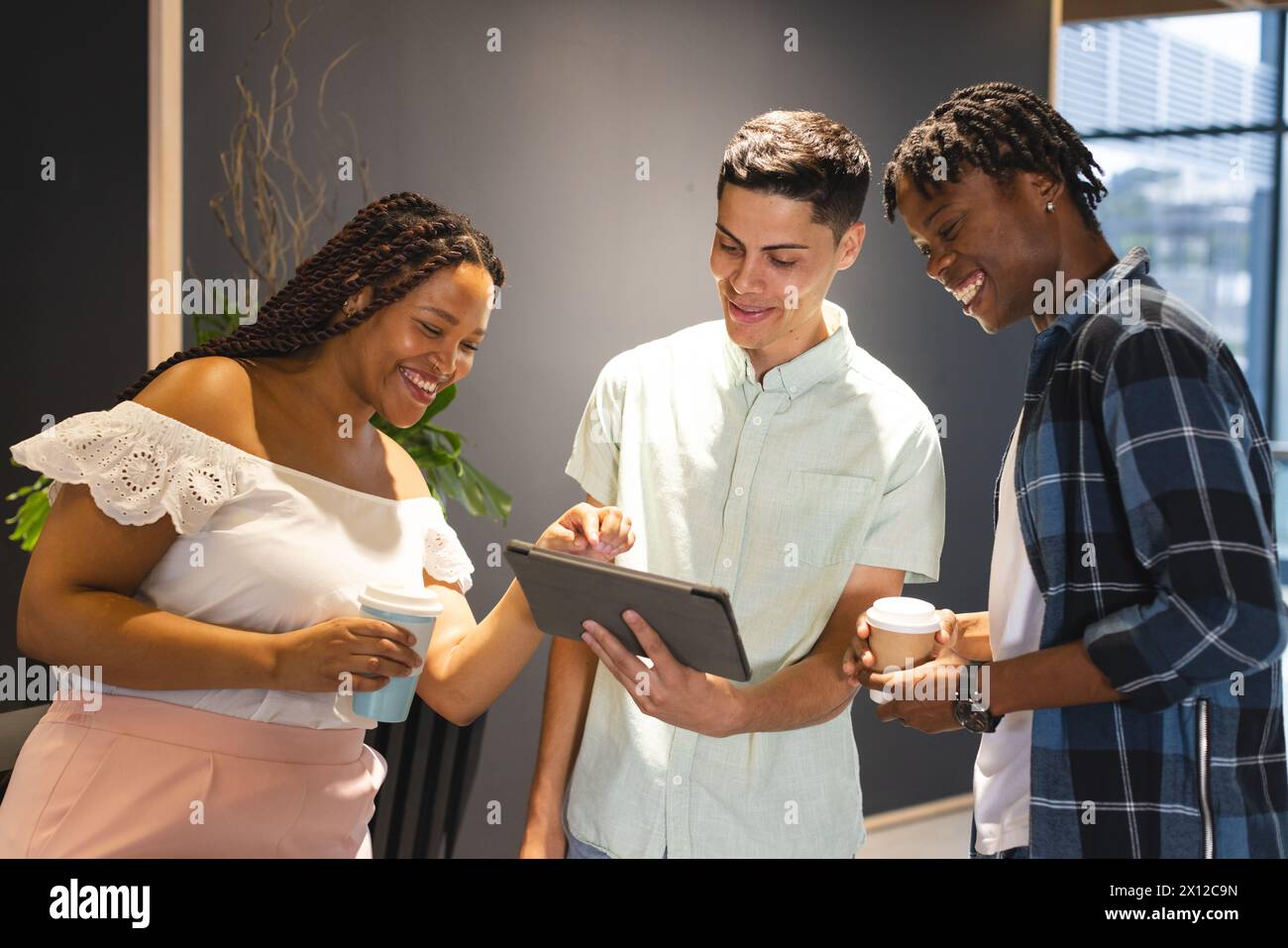 Un gruppo eterogeneo di colleghi che condividono un tablet e ridono insieme in un moderno ufficio aziendale Foto Stock